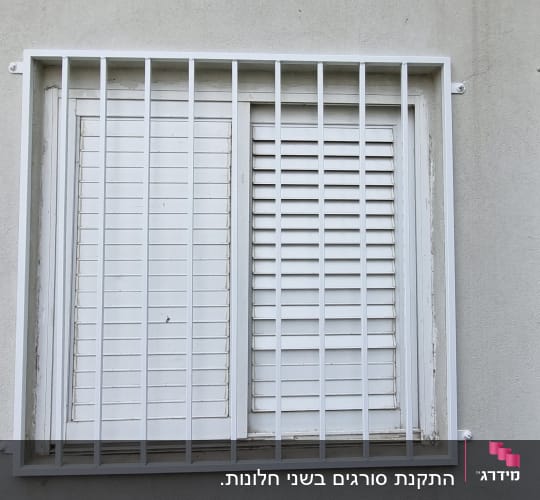 חלון עם סורגים לבנים על קיר אפור